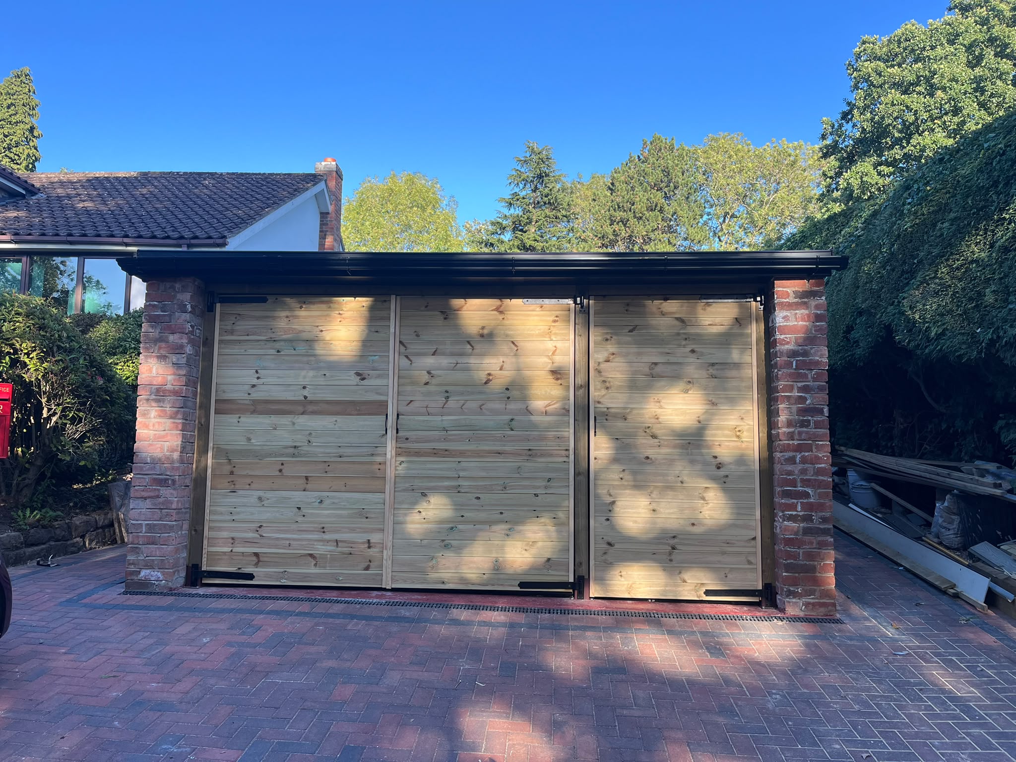 Timber-doored outbuilding with brick posts and a black fascia on a red block paved driveway